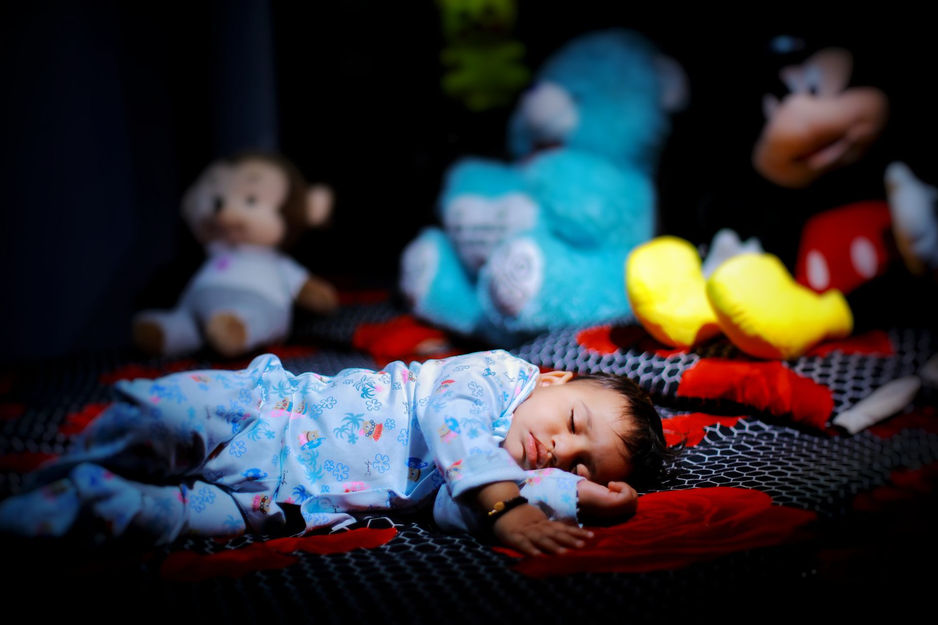 Een baby ligt slapend op zijn rug in zijn ledikant in een verduisterde kamer.